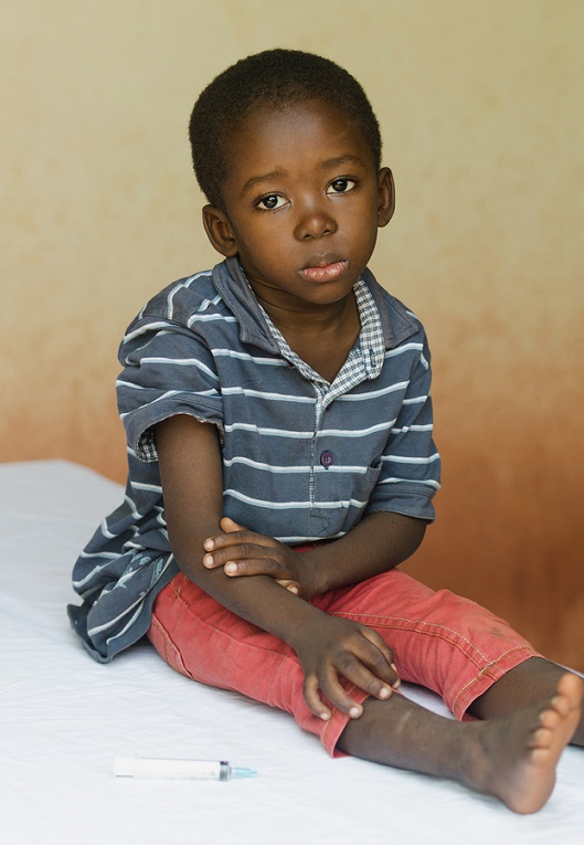Little boy sitting in a hospital waiting to get an injection. Symbol for African illness fighting. Black boy as a patient for a white woman nurse.